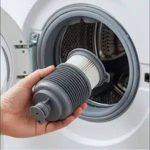 A person holds a washing machine pump filter in front of an open washing machine.