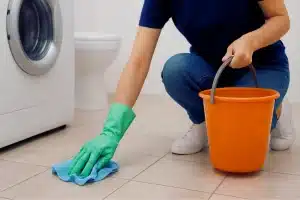 Person cleaning tiled floor with a cloth and bucket.